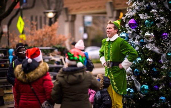 Buddy the Elf stands in front of a Christmas tree with children mimicking his motions at Hyde Park Holly Day